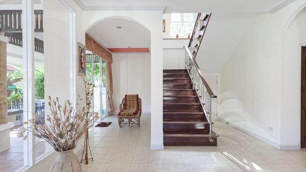 A spacious foyer with a staircase, a large vase with dried plants, and a wicker chair. - Karon Hill Villa (Karon)