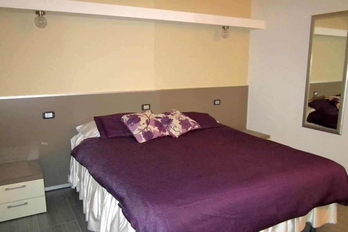 Ein Schlafzimmer mit einem Bett, einem Nachttisch, einer Kommode und einem Spiegel an der Wand.