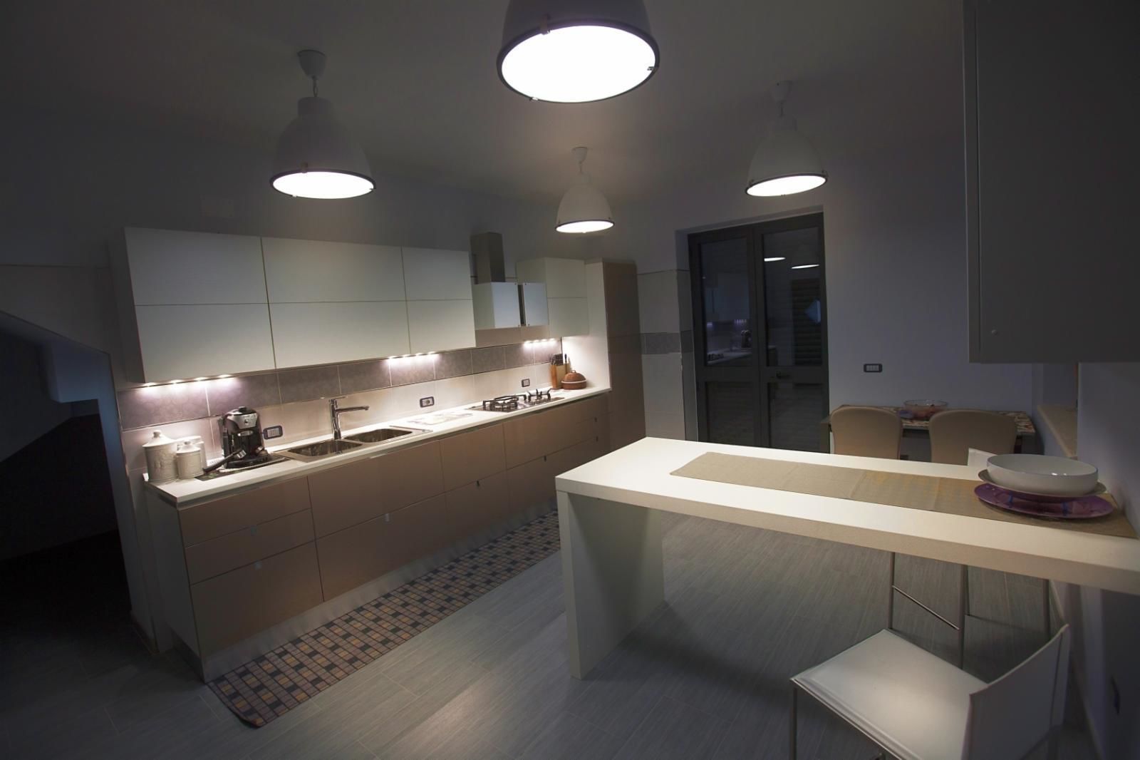 A modern kitchen with a central island, pendant lighting, and a view into the dining area.