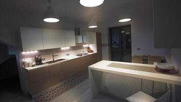 A modern kitchen with a central island, pendant lighting, and a view into the dining area.