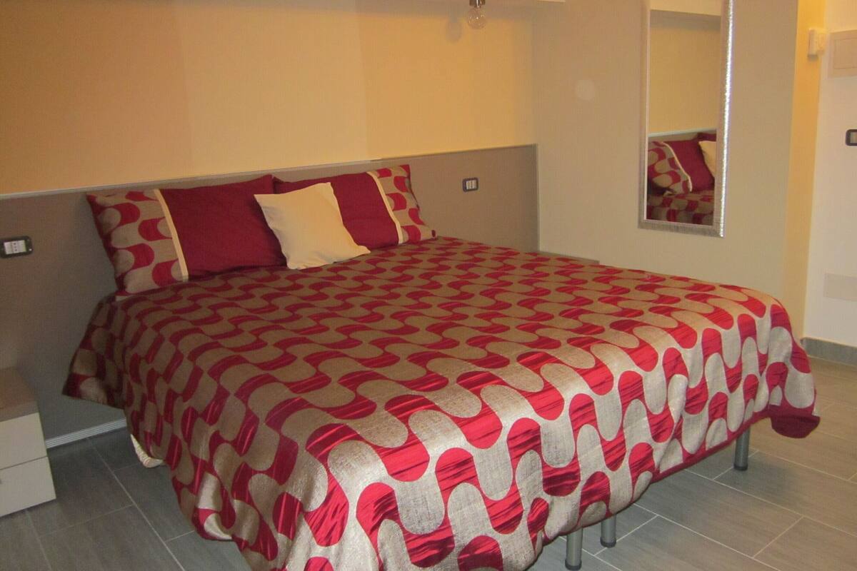 Ein Schlafzimmer mit einem gestreiften Bettüberwurf, einem Nachttisch und einem Spiegel an der Wand.