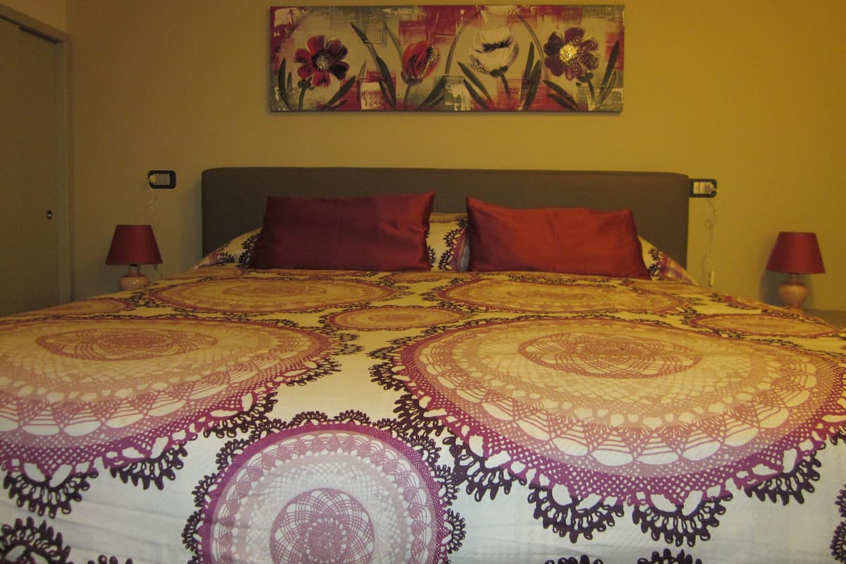 Ein Bett mit einem gemusterten Bettbezug, zwei rote Kissen und ein Blumenbild an der Wand.