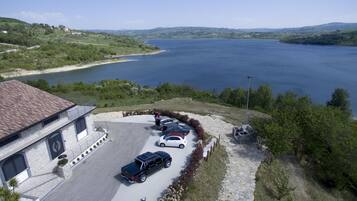 Un edificio de fachada de piedra, un estacionamiento con varios coches y vistas a un lago grande.