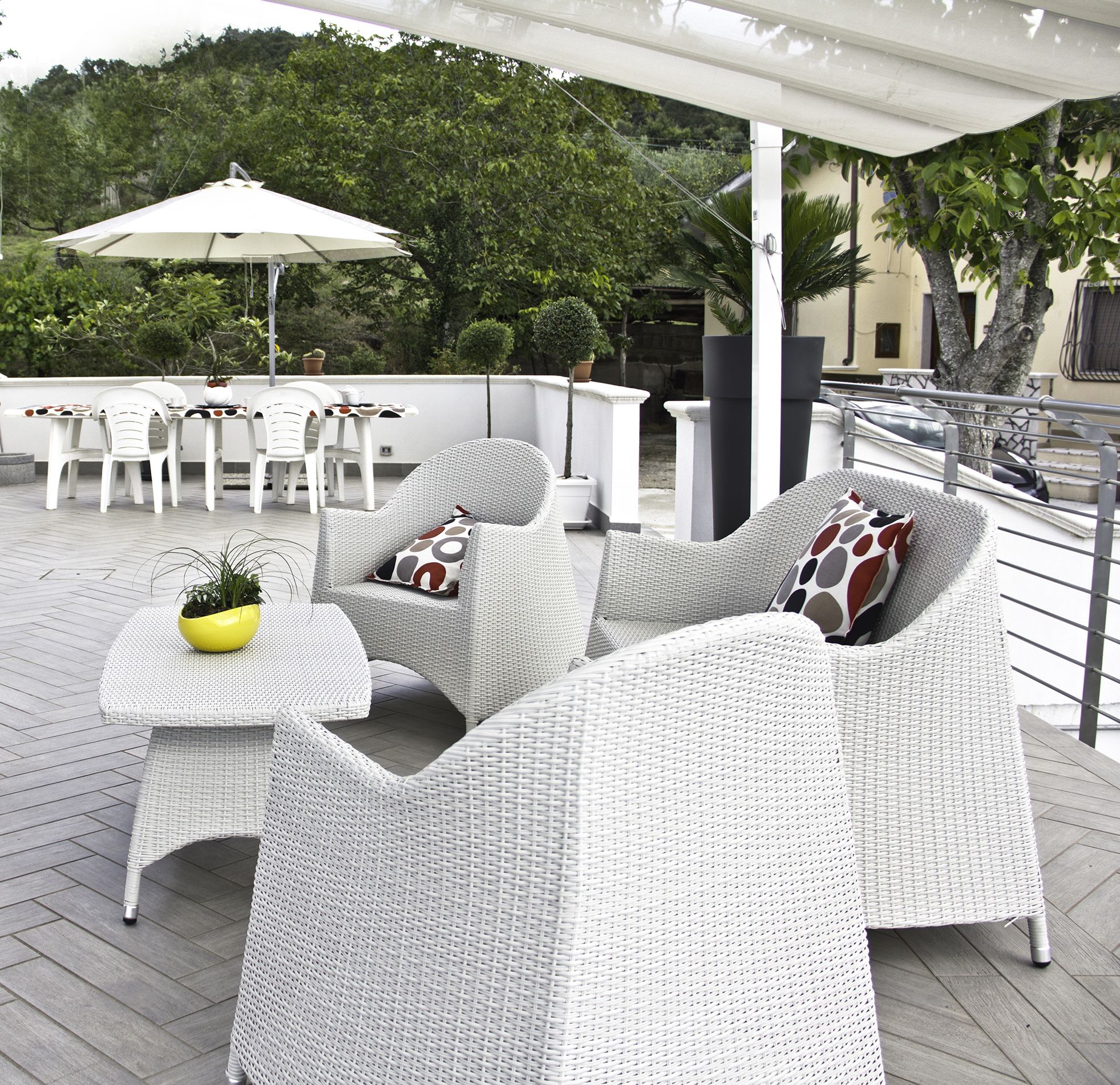 Eine Terrasse im Freien mit Korbmöbeln, einem weißen Sonnenschirm und Topfpflanzen.