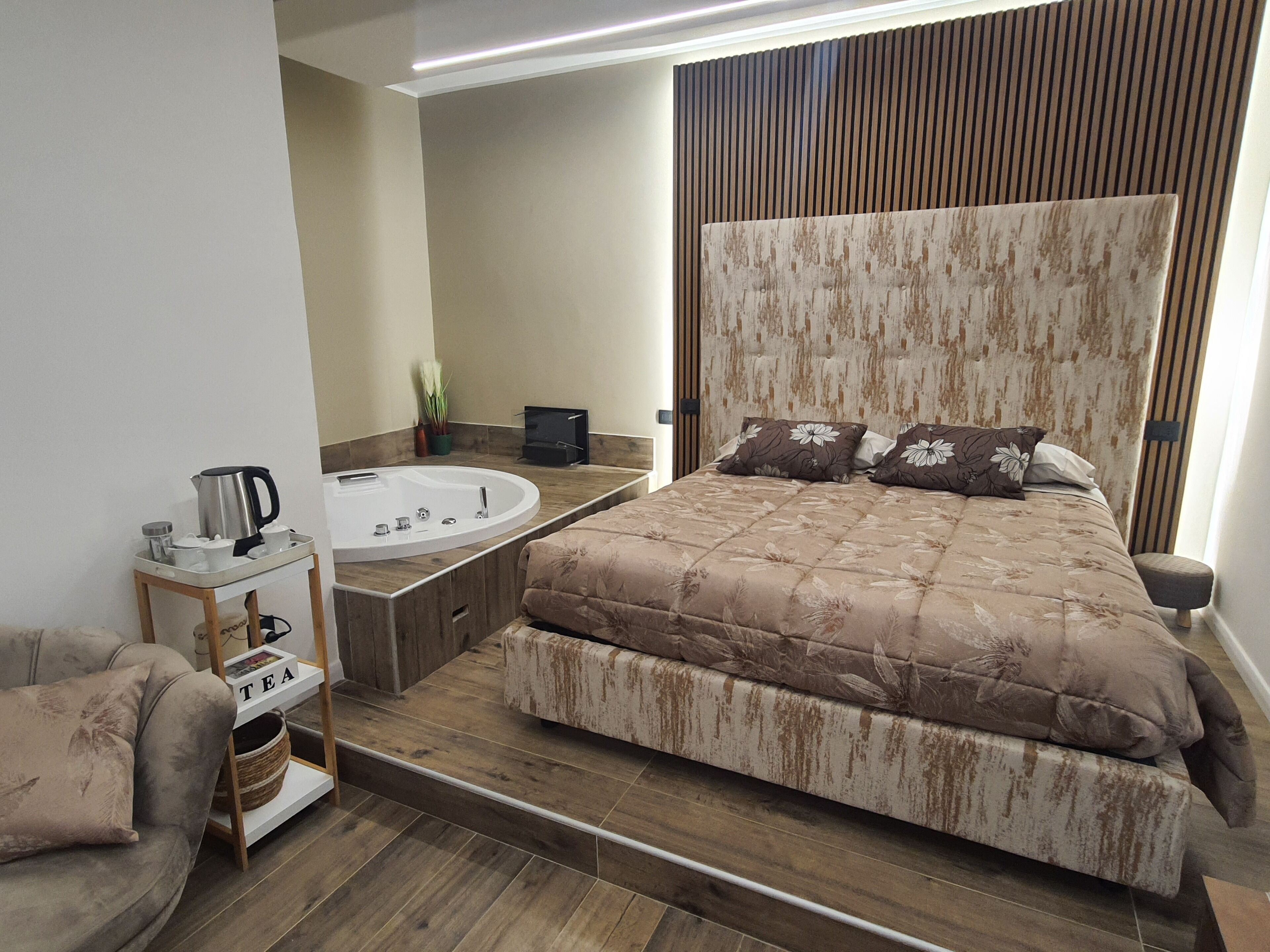 Een moderne slaapkamer met een groot bed, een inbouwbad en een klein nachtkastje met een waterkoker en bekers.