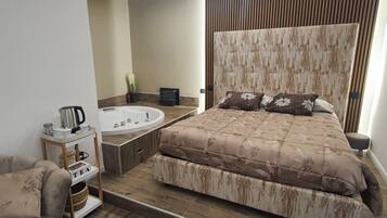 Een moderne slaapkamer met een groot bed, een inbouwbad en een klein nachtkastje met een waterkoker en bekers.