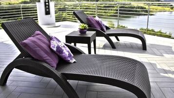 Een balkon met twee loungestoelen en een klein tafeltje, met uitzicht op een meer en groen.