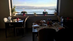 A dining area with a table set for two, a window with a view of a lake and hills, and potted plants on the windowsill.