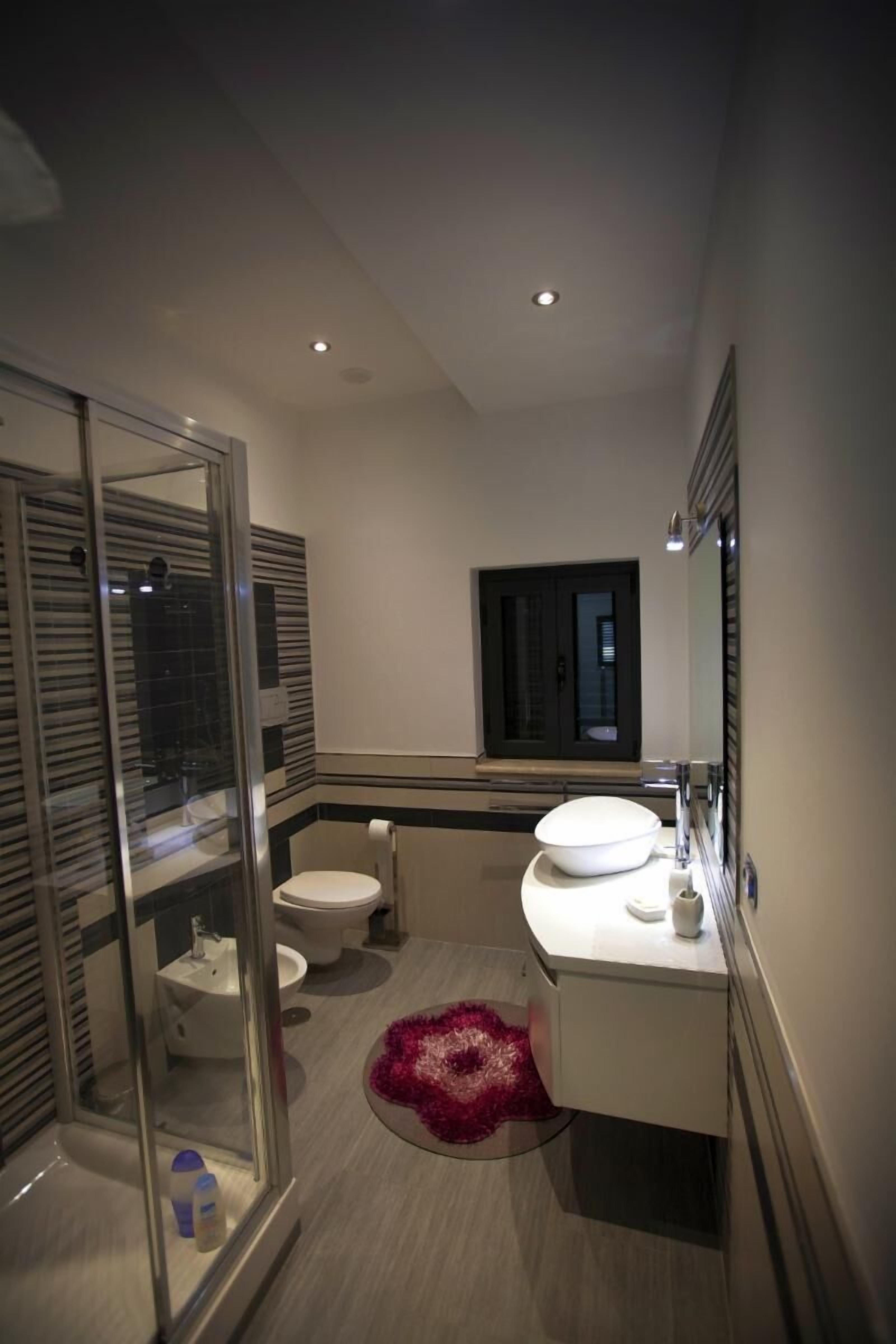 Een moderne badkamer met een douchecabine van glas, een witte wastafel en een toilet.