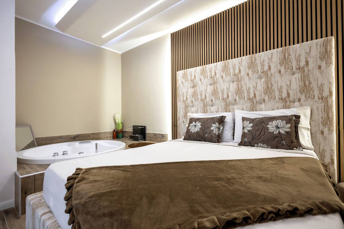 Ein modernes Hotelzimmer mit einem großen Bett, einem runden Badezimmer mit einer Badewanne und einer Wandpaneele aus Holz.