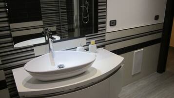 Un bagno moderno con un lavandino bianco grande, uno specchio e una doccia.