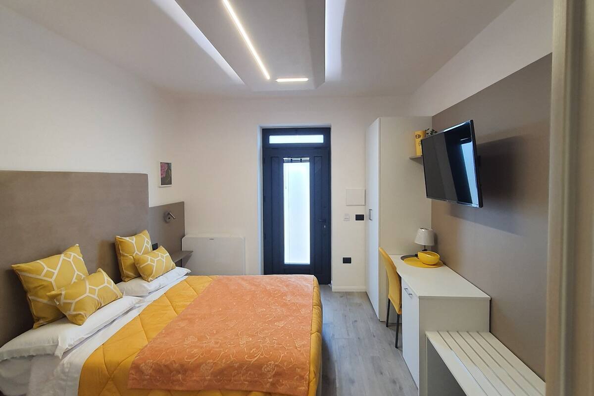 Ein modernes Hotelzimmer mit Bett, Nachttisch, Fernseher und Schreibtisch mit Stuhl.