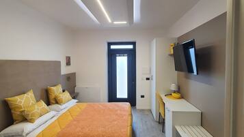 Una habitación de hotel moderna con cama, mesita de noche, televisor y escritorio con silla.