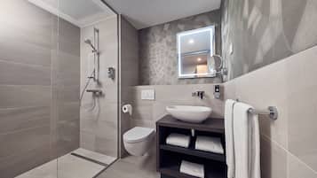 A modern bathroom with a glass shower enclosure, a toilet, a sink with a vessel basin, and a towel rack.