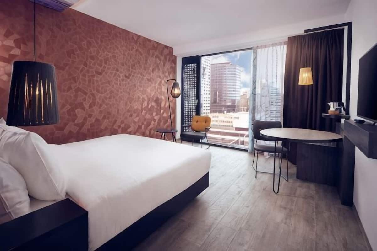 A hotel room with a bed, a desk, a chair, a TV, and a city view.