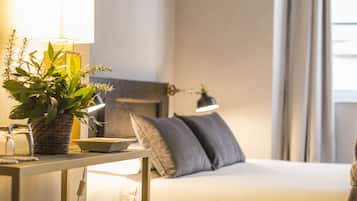 A bedroom with a bed, bedside table, lamp, and a potted plant.