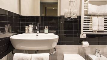 A modern bathroom with a large sink, toilet, and bathtub. There are towels and toiletries on the sink and a towel rack above the bathtub.