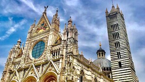 A Gothic-style cathedral with intricate architectural details, a prominent clock tower, and a large rose window. - PALAZZO DEL PAPA  (Siena)