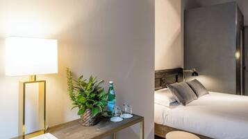 A hotel room with a bed, bedside table, lamp, and a small potted plant.