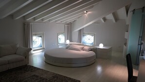 Et moderne soveværelse med en rund seng, store vinduer, en sofa og et lille bord.