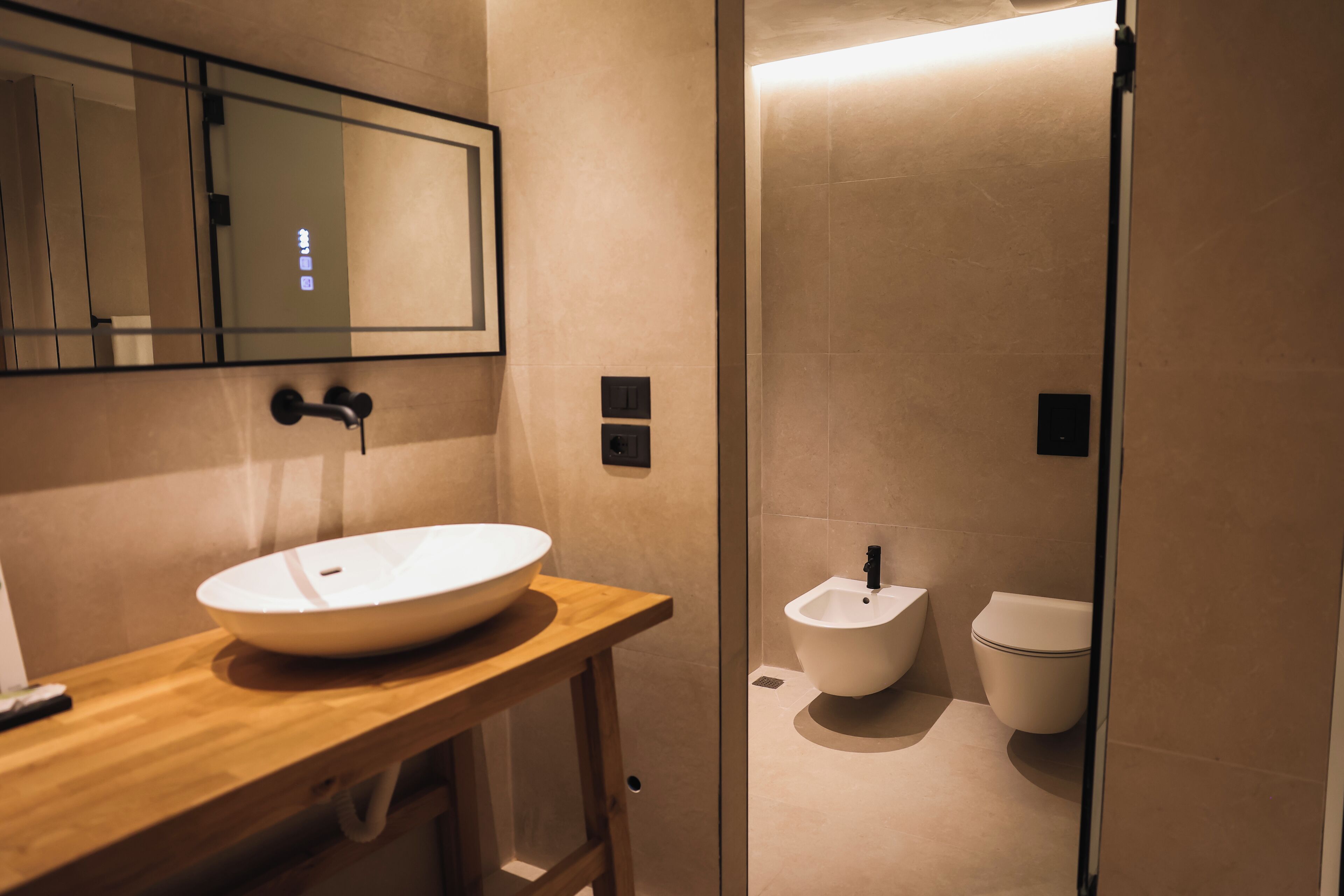 Un baño moderno con tocador de madera, un lavamanos grande y blanco, un bidé y un inodoro.