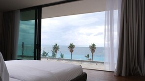 Ein Schlafzimmer mit einem großen Bett, einer Schiebetür zu einem Balkon mit Blick auf das Meer und Palmen.