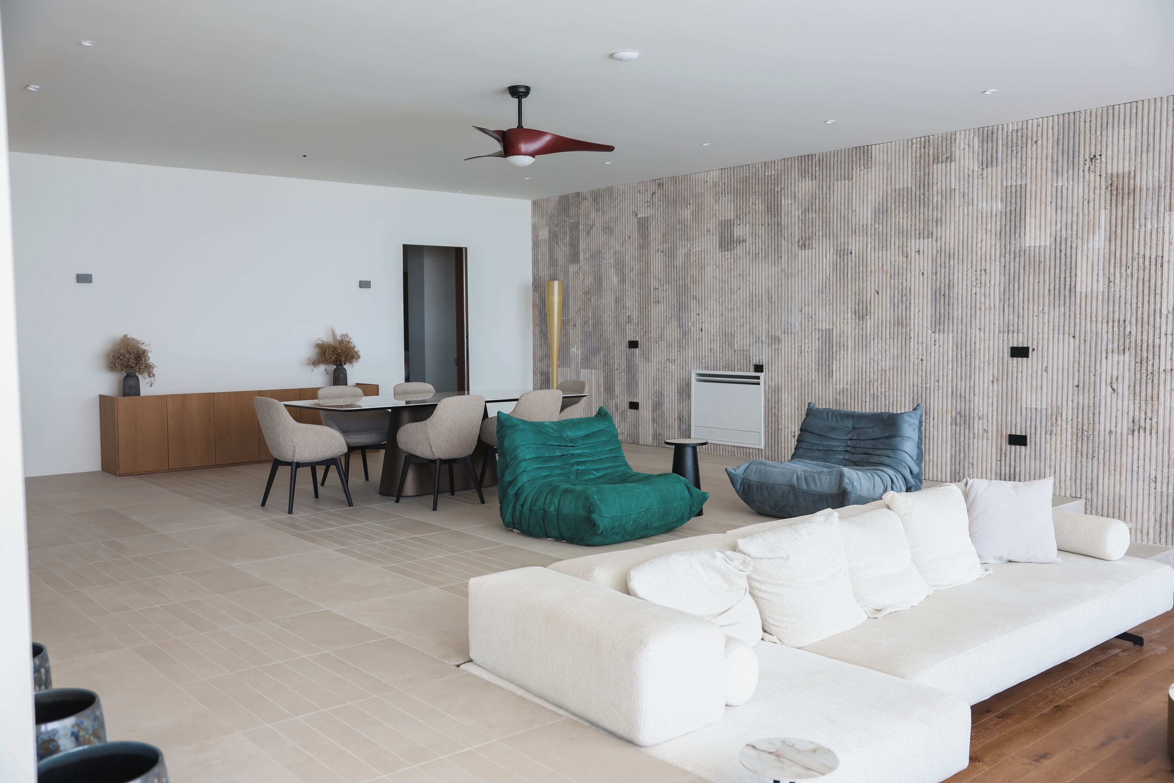 Een moderne woonkamer met een witte bank, blauwgroene en blauwe fauteuils, een eethoek met een tafel en stoelen, en een structuurwand.