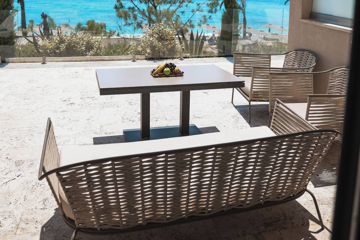 Een terras met een tafel en stoelen, met uitzicht op een strand en de zee.