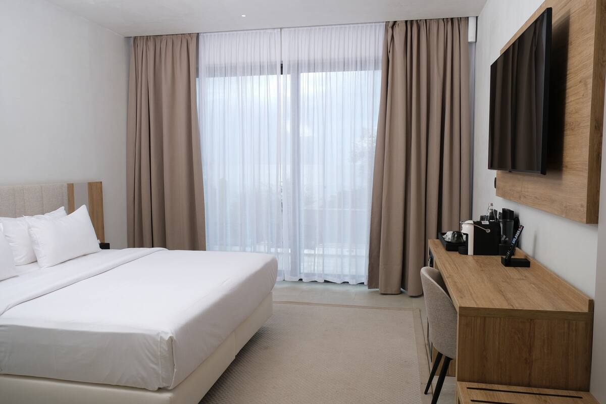 Een hotelkamer met een groot bed, een houten bureau, een flatscreen televisie en een groot raam met gordijnen.