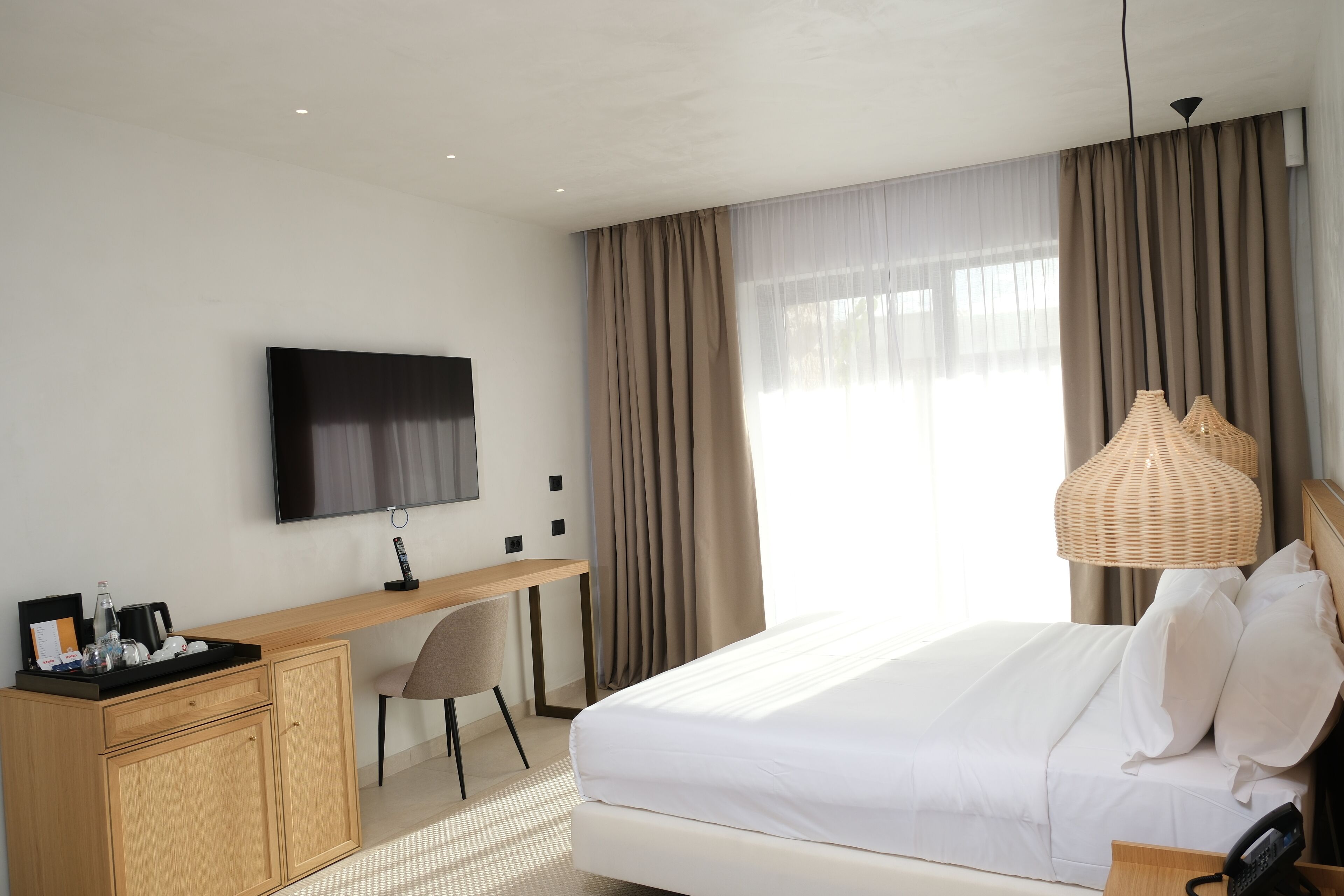 A hotel room with a bed, a desk, a chair, a TV, and a lamp.