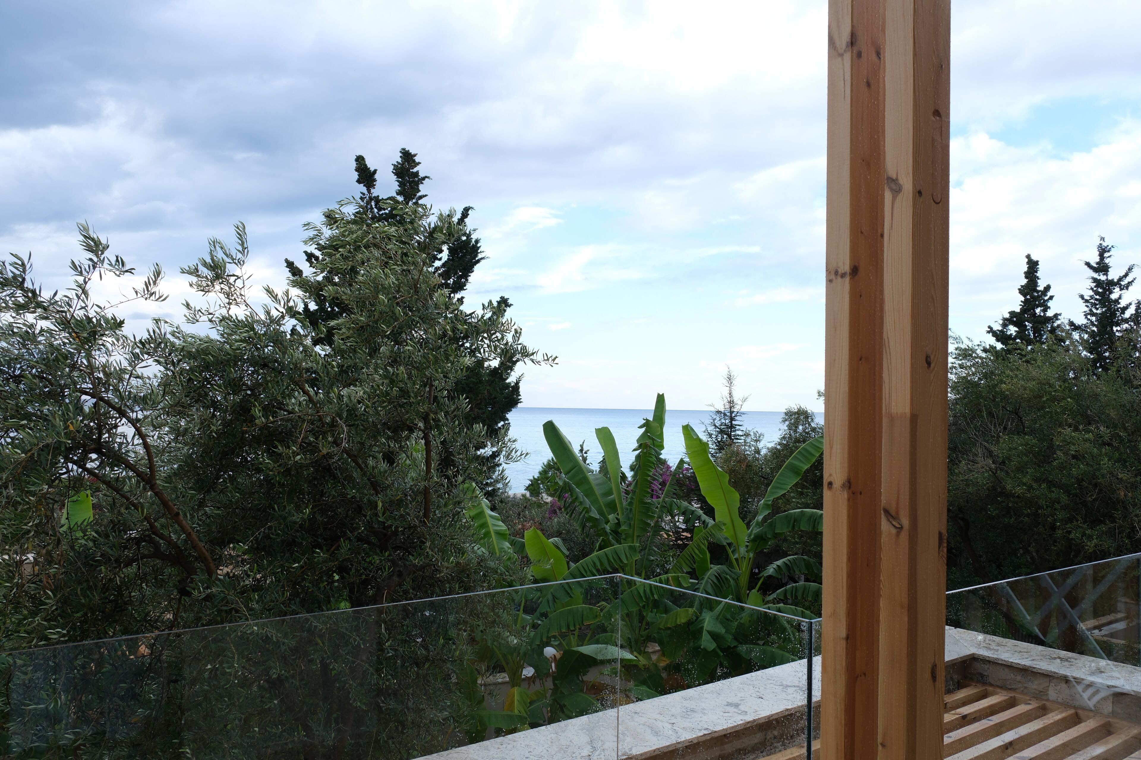 Barandal de madera con vista a un jardín exuberante y al mar.