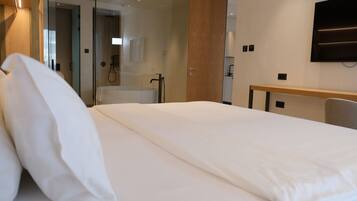 Une chambre d’hôtel avec un grand lit, un bureau en bois et un téléviseur fixé au mur.