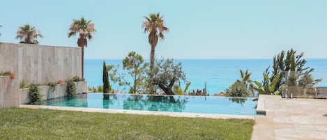 A swimming pool with a view of the sea, surrounded by palm trees and a wooden fence.