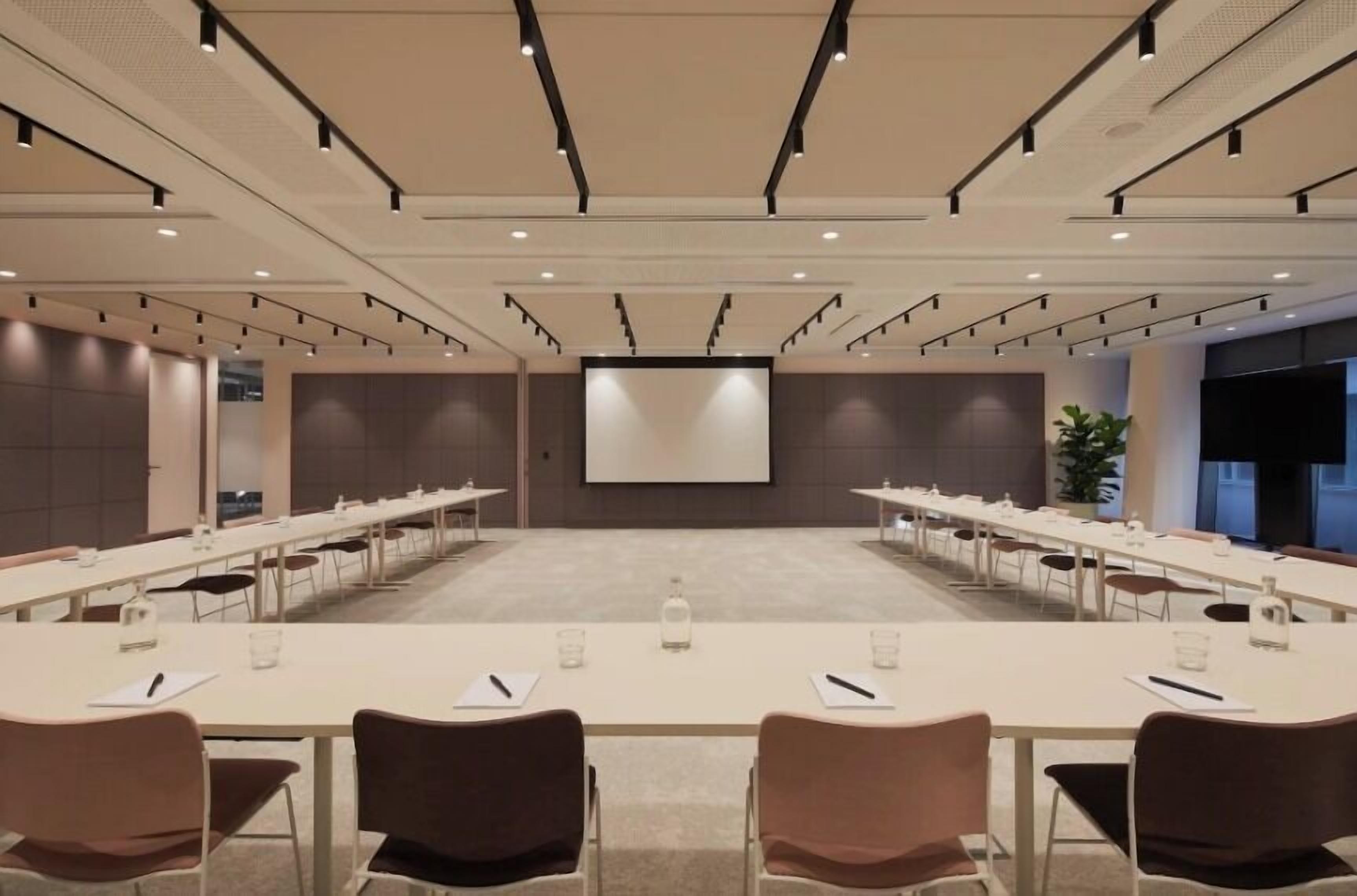 A conference room with a long table, chairs, a projector screen, and a large screen.
