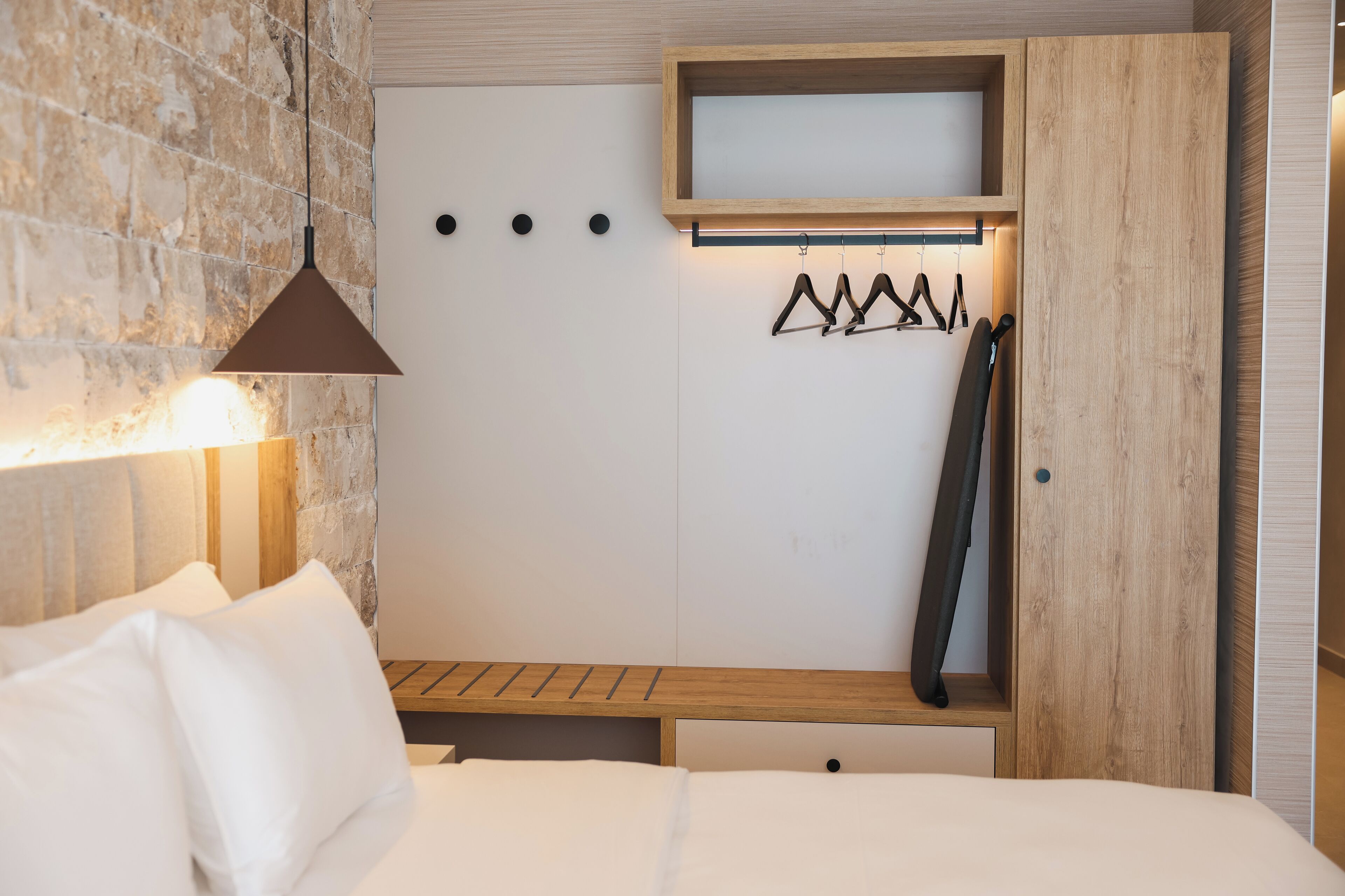 A bedroom with a bed, a hanging light, a wooden shelf, and a coat rack.