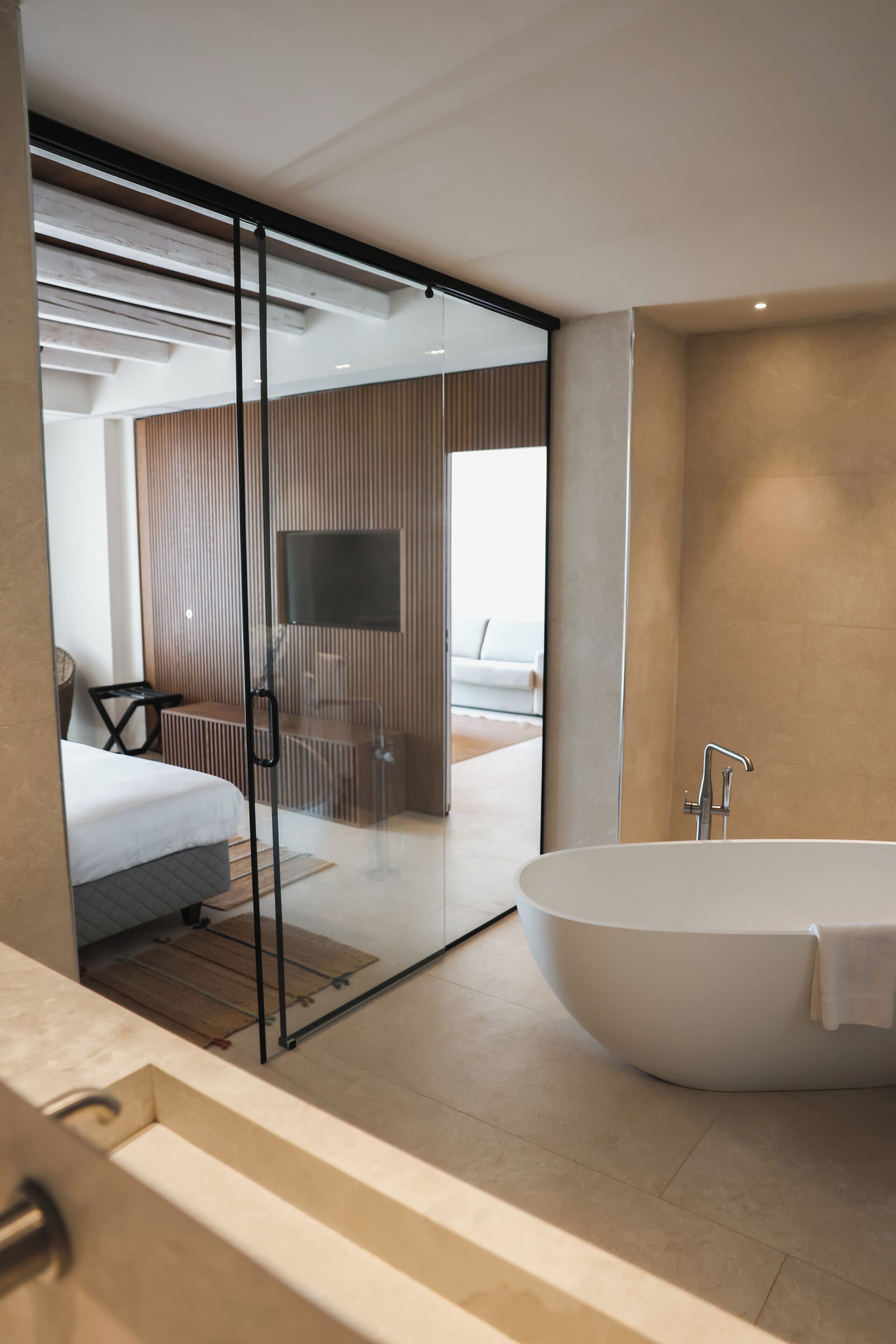A modern bathroom with a freestanding bathtub, a glass shower enclosure, and a visible TV in the adjacent room.