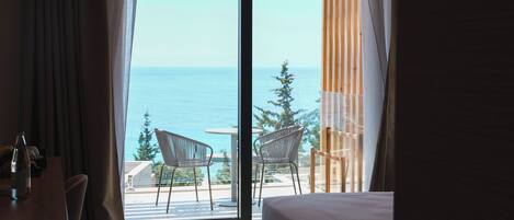 Habitación de hotel con un gran ventanal corredero que da a un balcón con vistas al mar y a árboles.