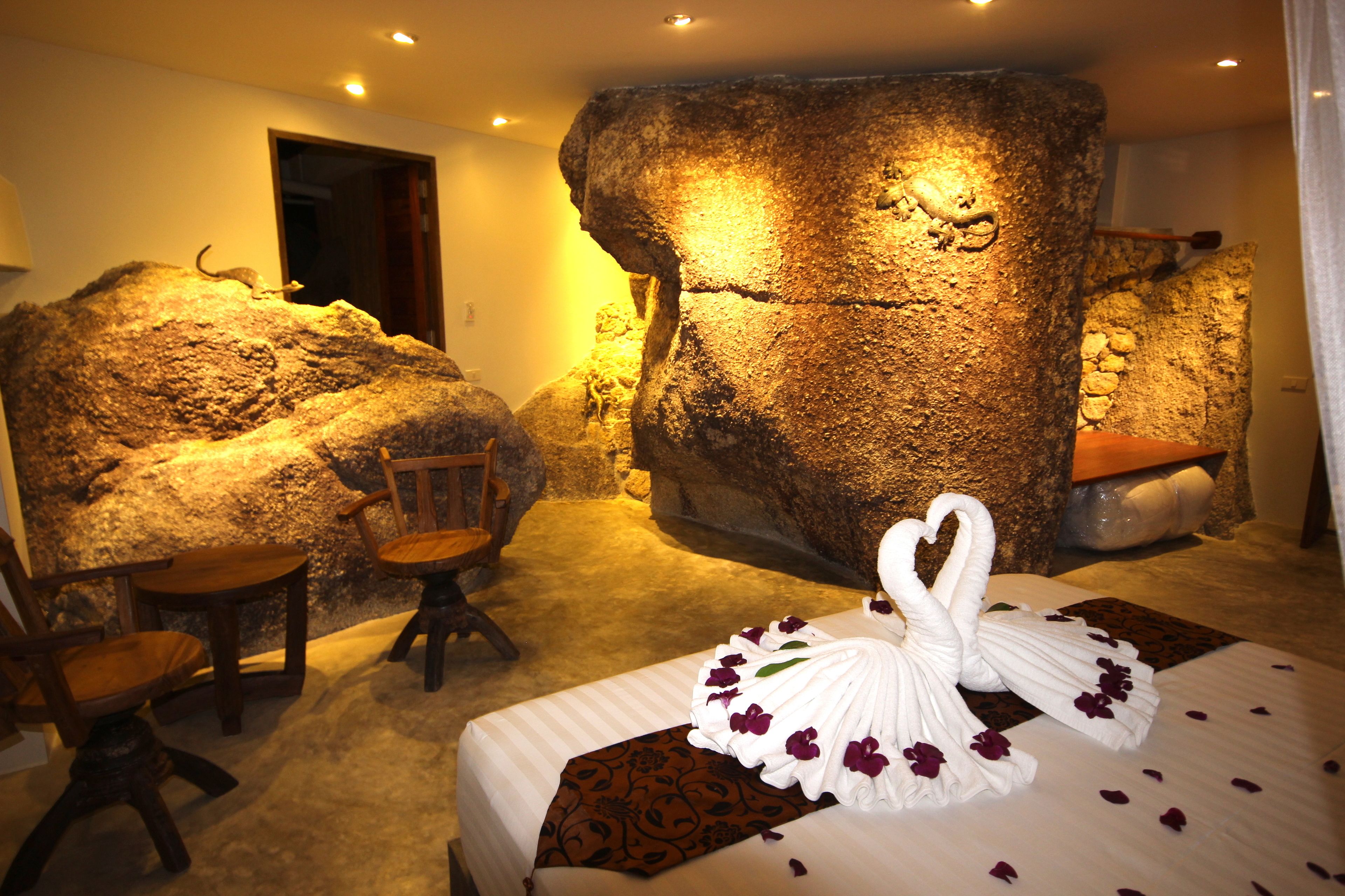 Una habitación con una pared de roca grande, una cama con una toalla con forma de cisne y una silla.