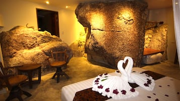 Una habitación con una pared de roca grande, una cama con una toalla con forma de cisne y una silla.