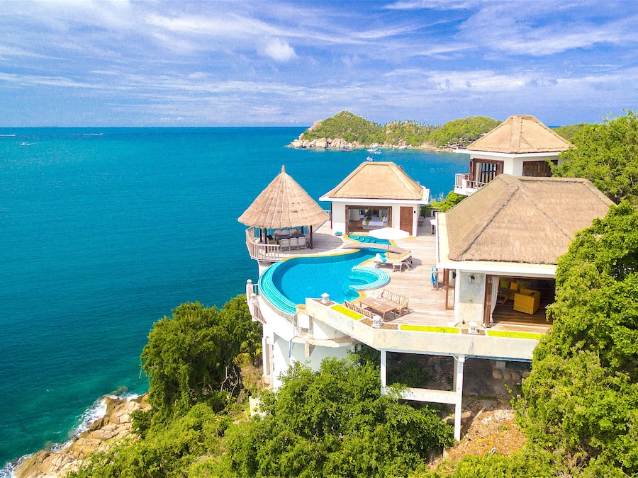 A resort with a large swimming pool, thatched-roof structures, and ocean views.