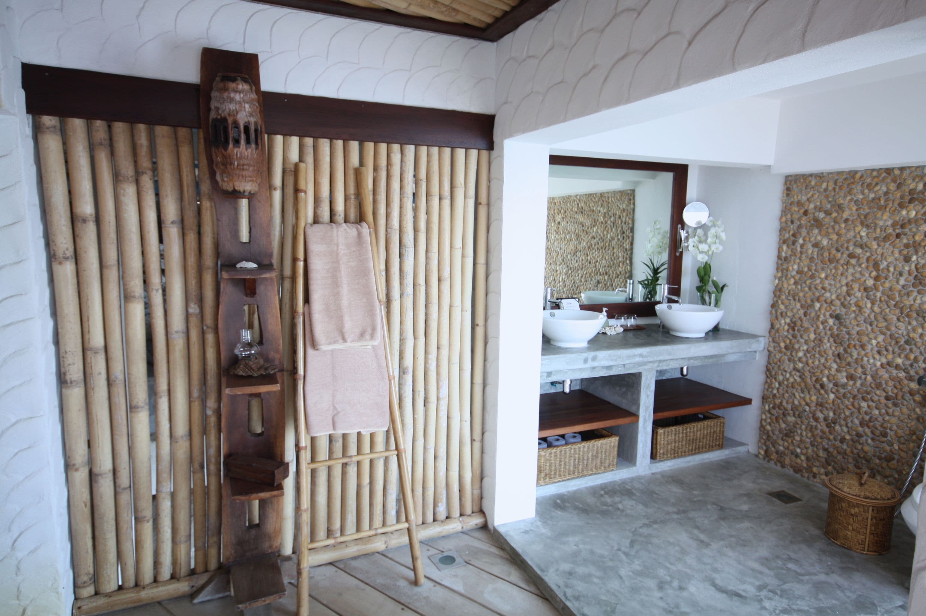 Un baño con pared de bambú, una escalera de madera, un lavabo, un espejo y una pared de piedra.