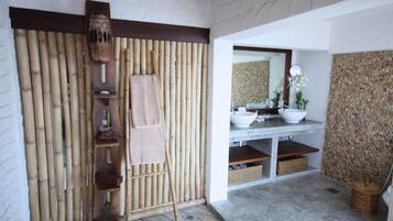 Un baño con pared de bambú, una escalera de madera, un lavabo, un espejo y una pared de piedra.