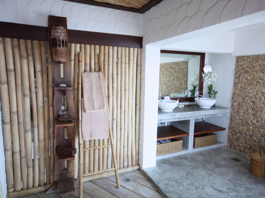 Un baño con pared de bambú, una escalera de madera, un lavabo, un espejo y una pared de piedra.