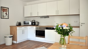 A modern kitchen with white cabinets, stainless steel appliances, and a wooden dining table with a vase of flowers. - Modernes Apartmenthaus (Falkensee)