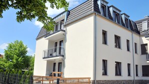 A modern two-story building with a balcony, a fenced courtyard, and a clear sky. - Modernes Apartmenthaus (Falkensee)