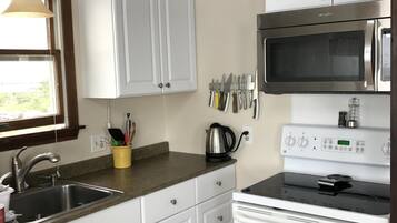 A kitchen with white cabinets, a stainless steel microwave, an oven, a sink, and a window with blinds.