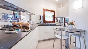 A modern kitchen with a central island, built-in appliances, and a window with a decorative curtain. - Ossuccio Villa Darsena private lakeside villa with pool by Italian Apartments. (Ossuccio)