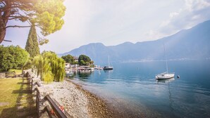 A lakeside view with boats, a wooden walkway, and mountains in the background. - Ossuccio Villa Darsena private lakeside villa with pool by Italian Apartments. (Ossuccio)