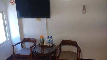 A room with a television mounted on the wall, a small table with chairs, and a trash bin.