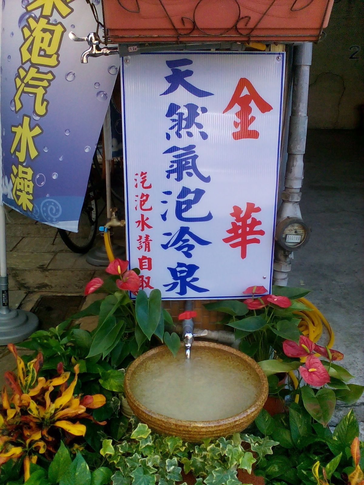Uma placa com caracteres chineses, uma fonte de água e um banner com caracteres chineses.